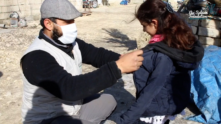 A volunteer putting a coat on a child as part of the warmth project clothing bundles.