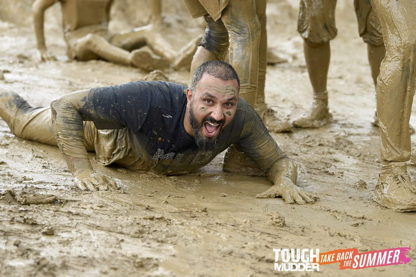 A man crawling in the mud as part of a charity tough mudder event.