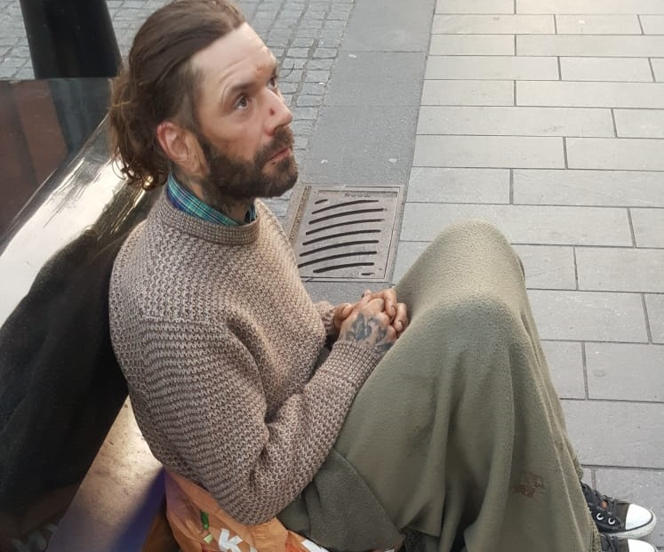 A homeless man sat on the ground with a blanket wrapped around him