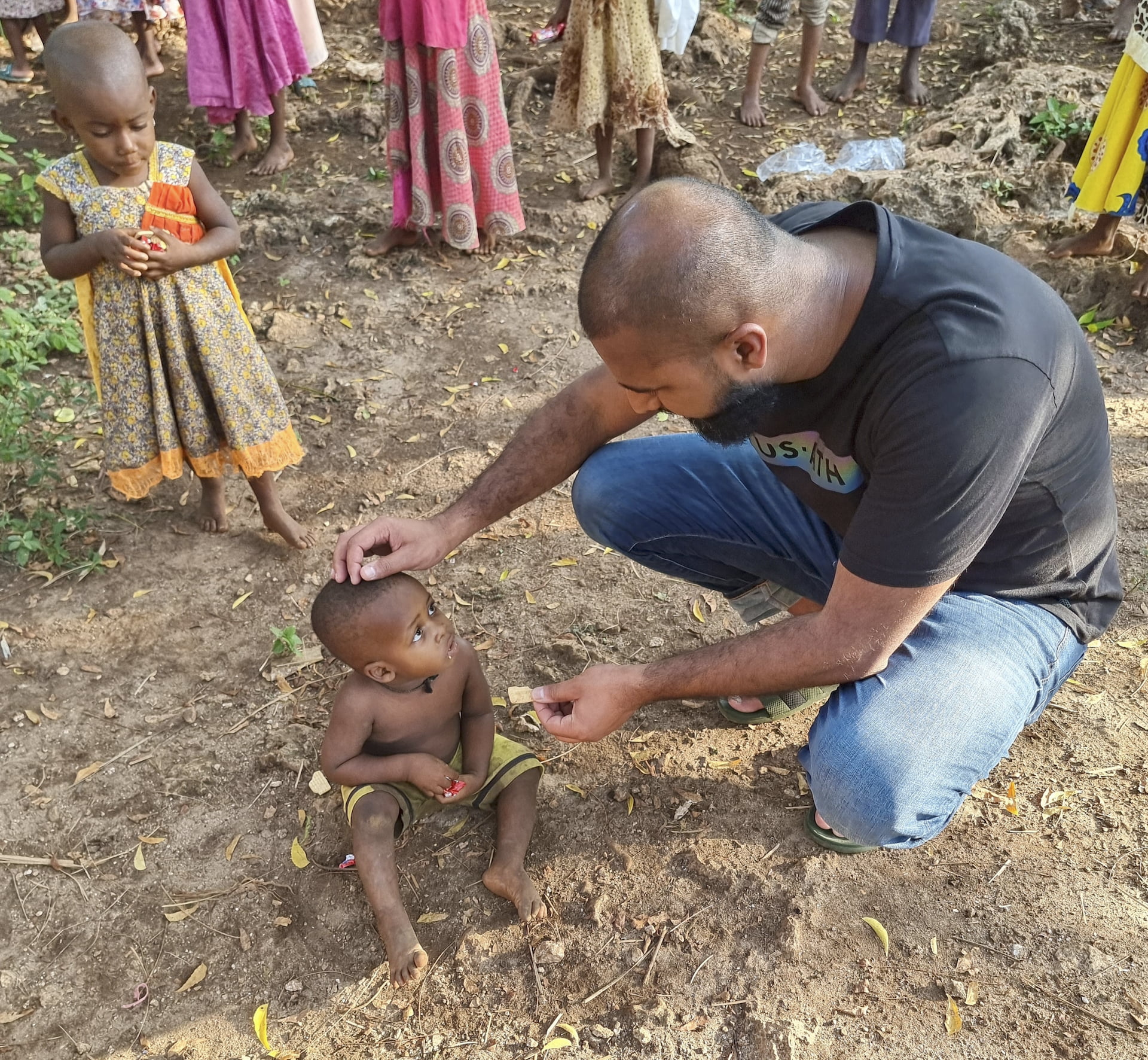A man kneeled down offering food to a poor child sat in the dirt