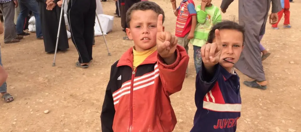 2 young orphans looking at the camera with their index fingers pointed to the sky